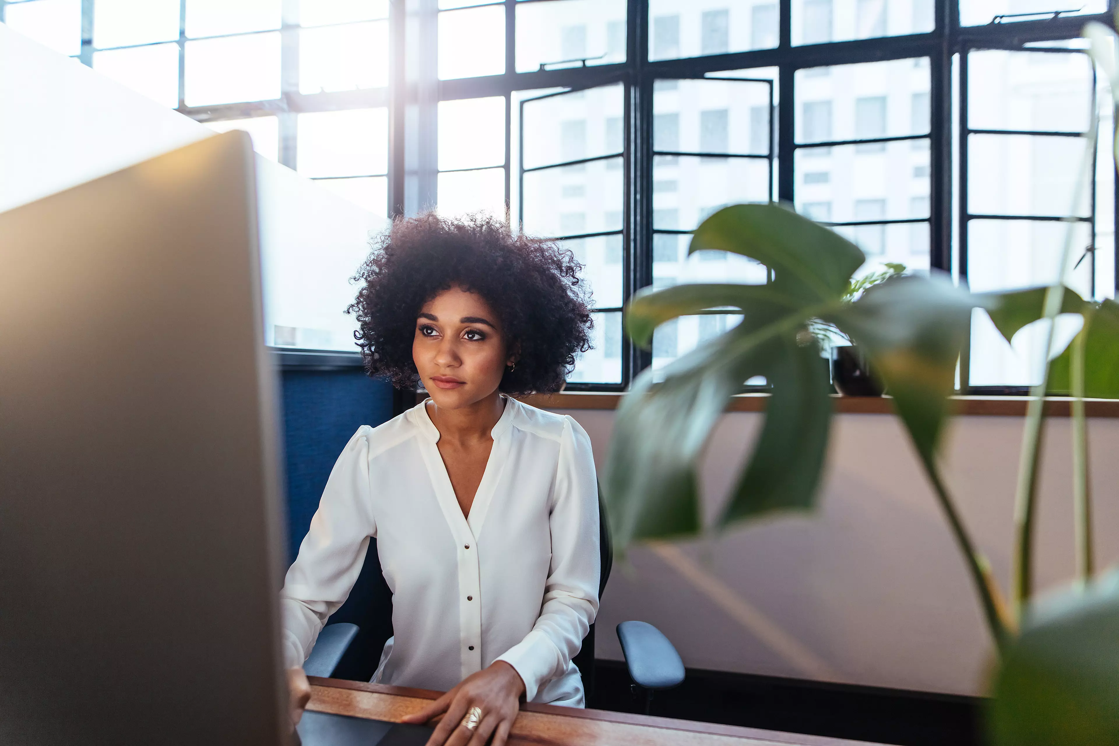  Dark haired woman sitting behind a desk, working on her desktop computer.