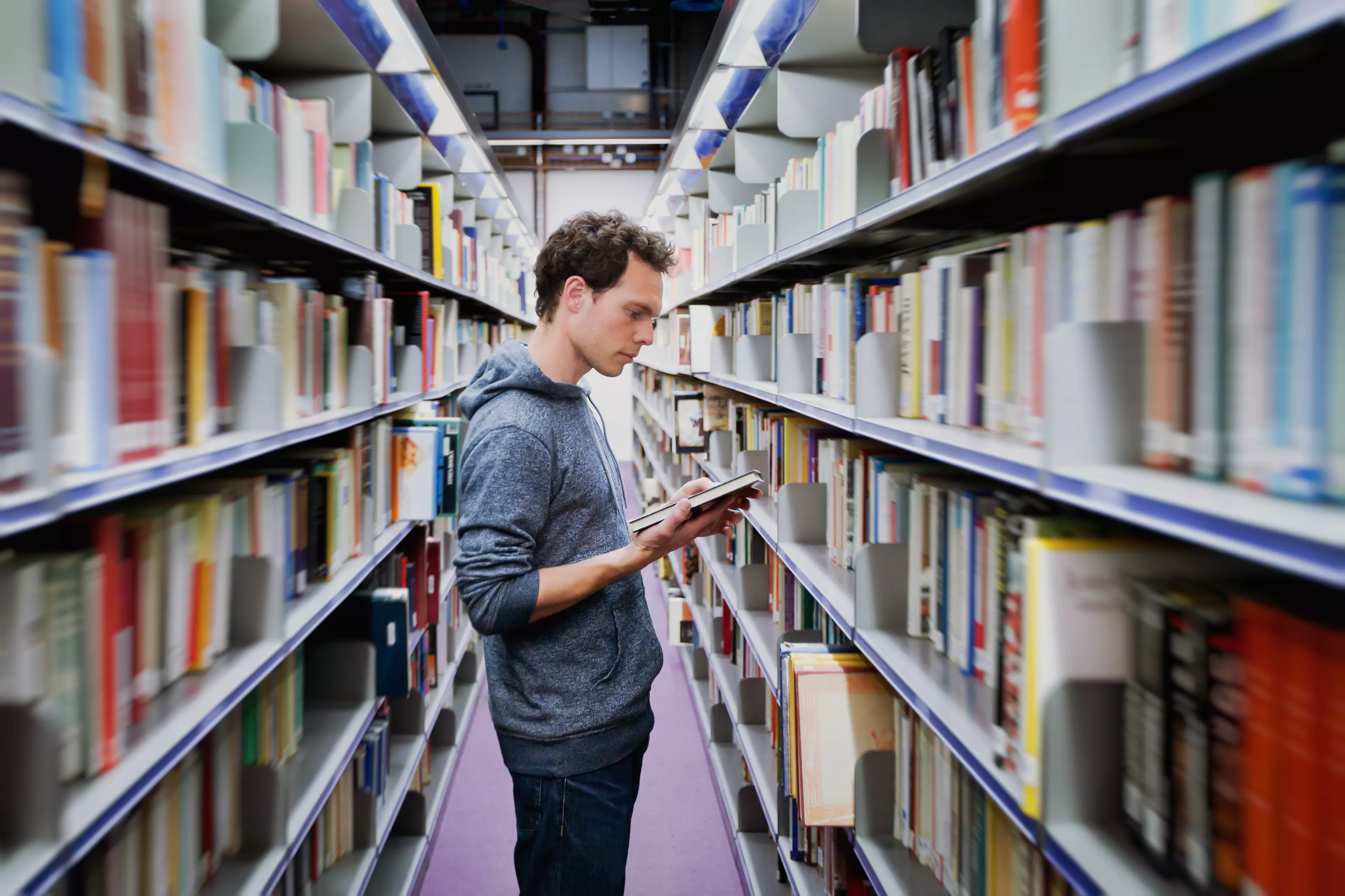 Young student reading a book between library shelves