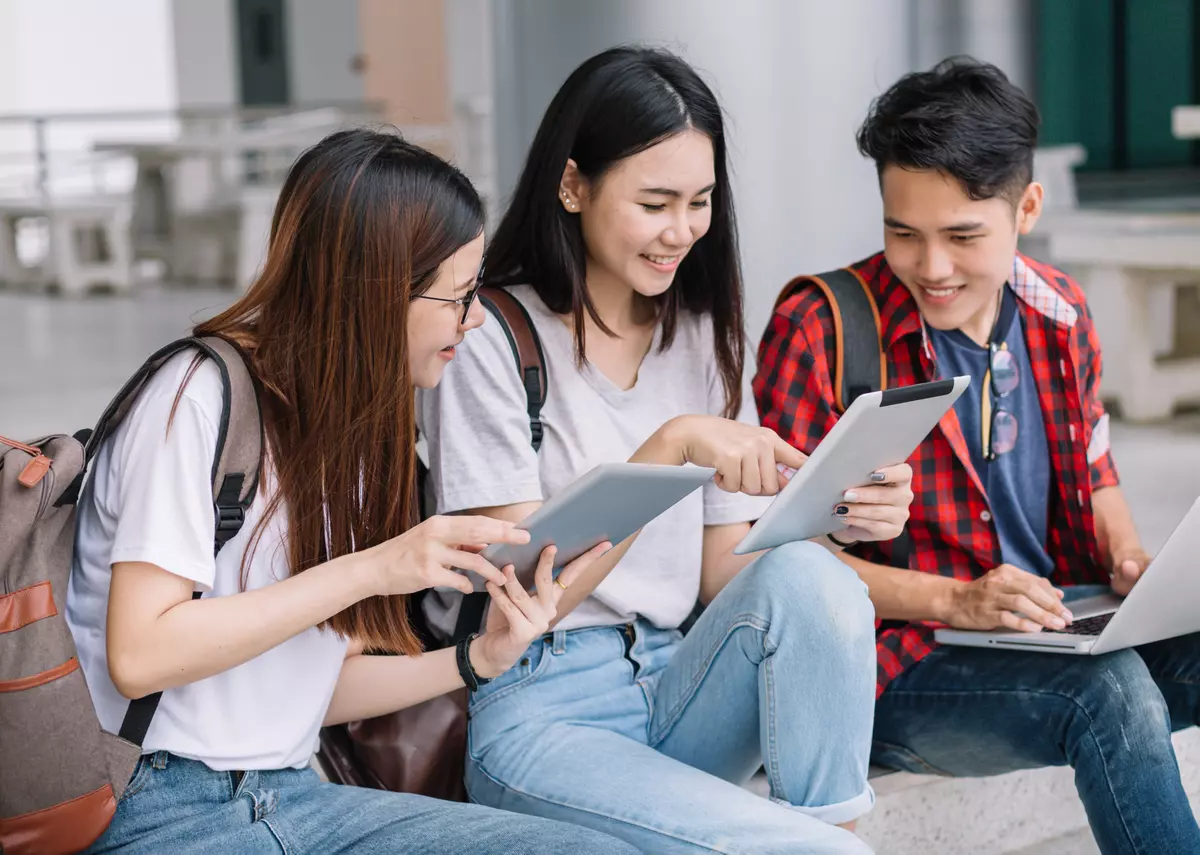 Teenagers sitting together, looking at their laptop and tablets.