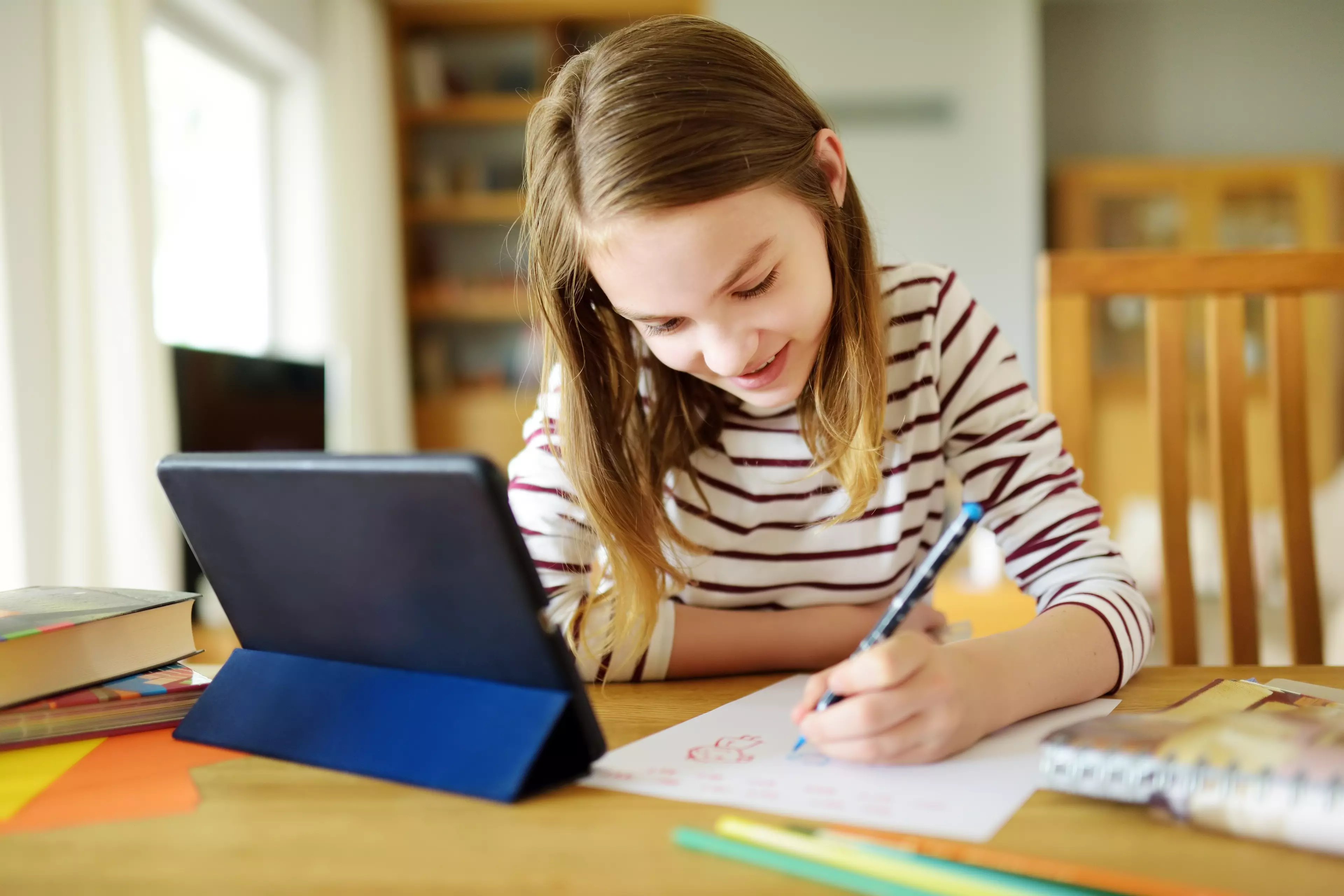 Młoda uczennica siedzi przed tabletem i notuje podczas lekcji online.