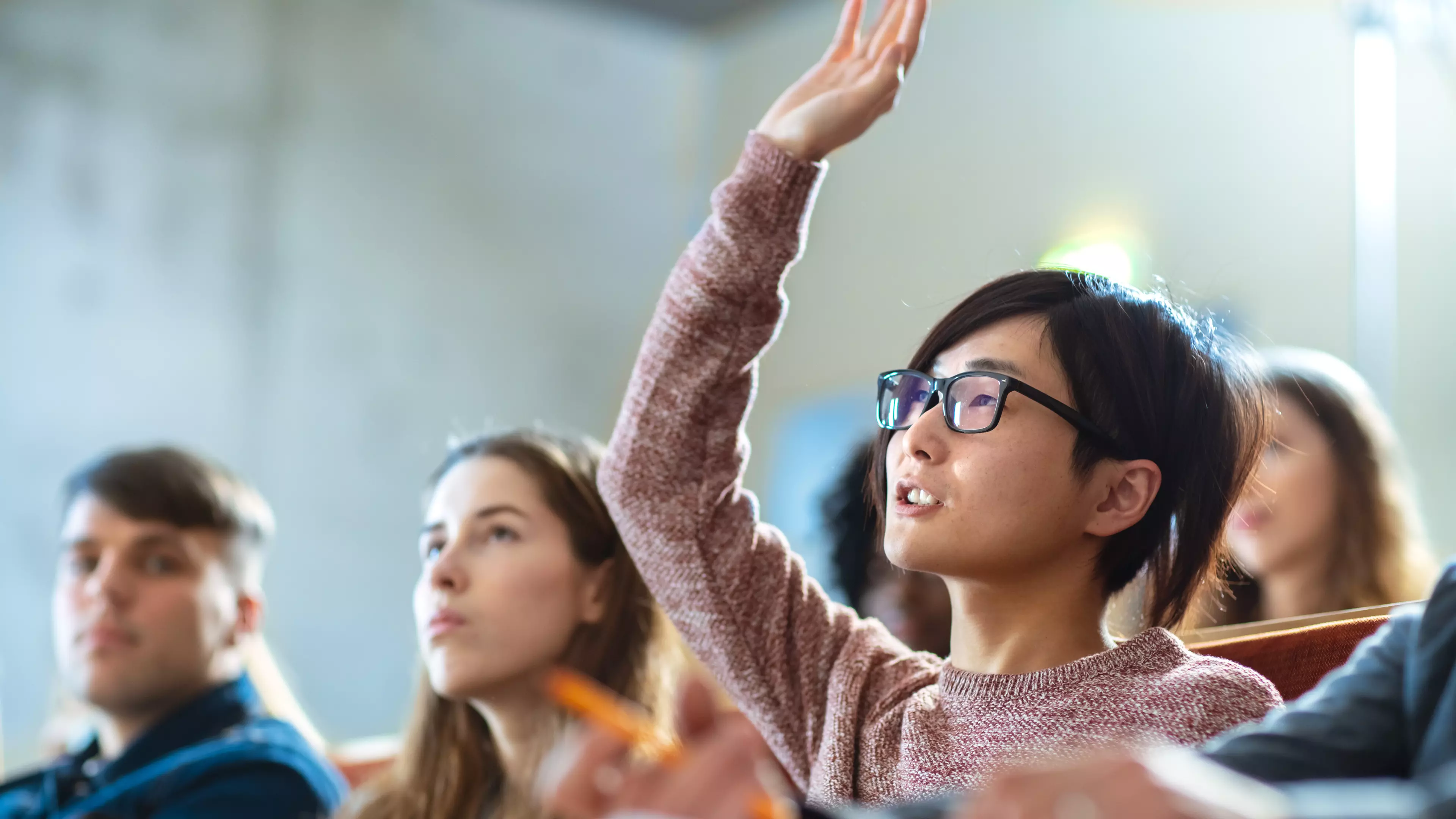 Young, short-haired woman in glasses raising hand to ask a question.