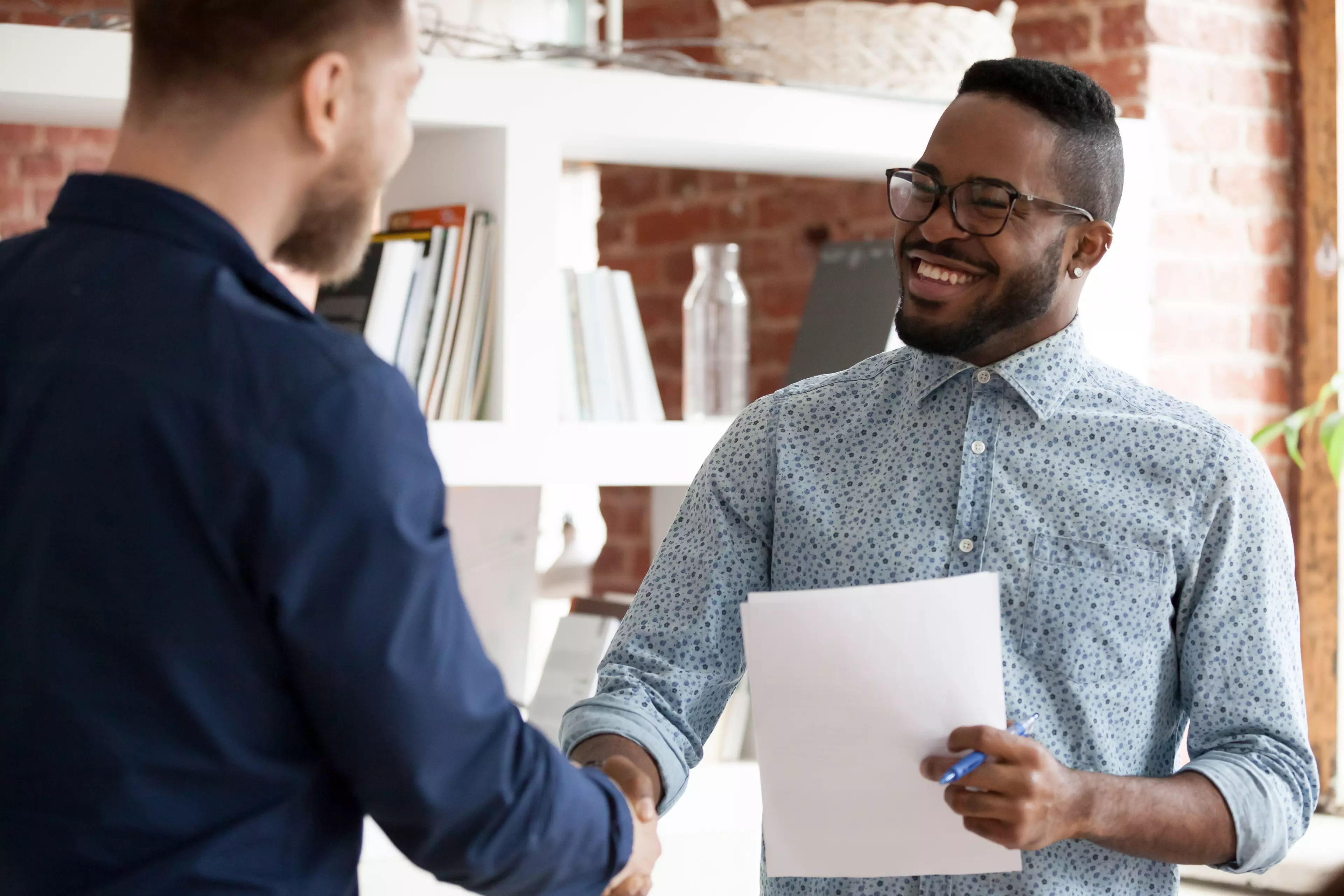  Two men in the office environment, facing each other and shaking hands.