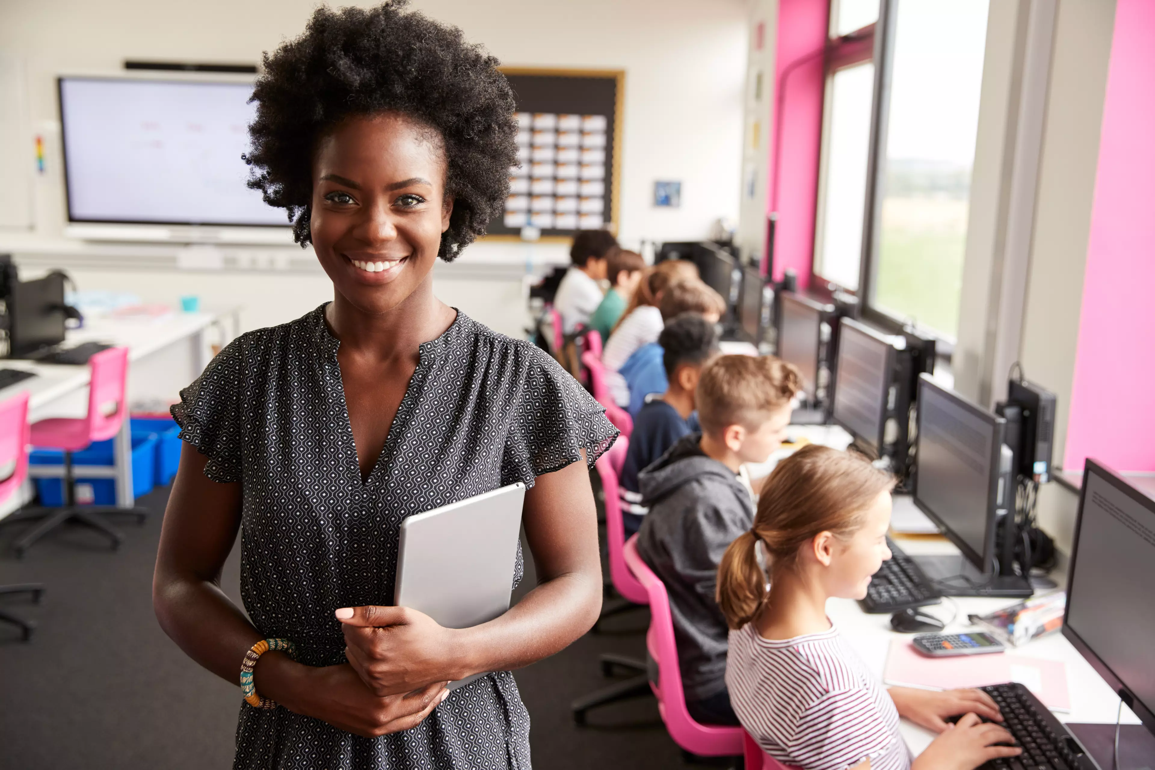 Smiling african-american woman teacher with young pupils during ICT class