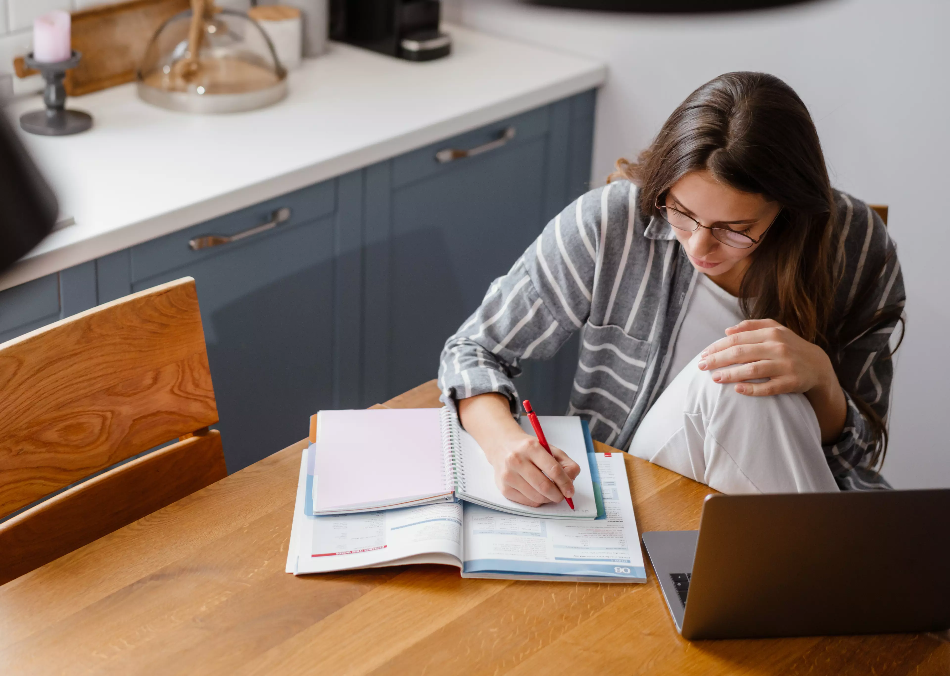  A woman sitting at a table in a kitchen, making notes.