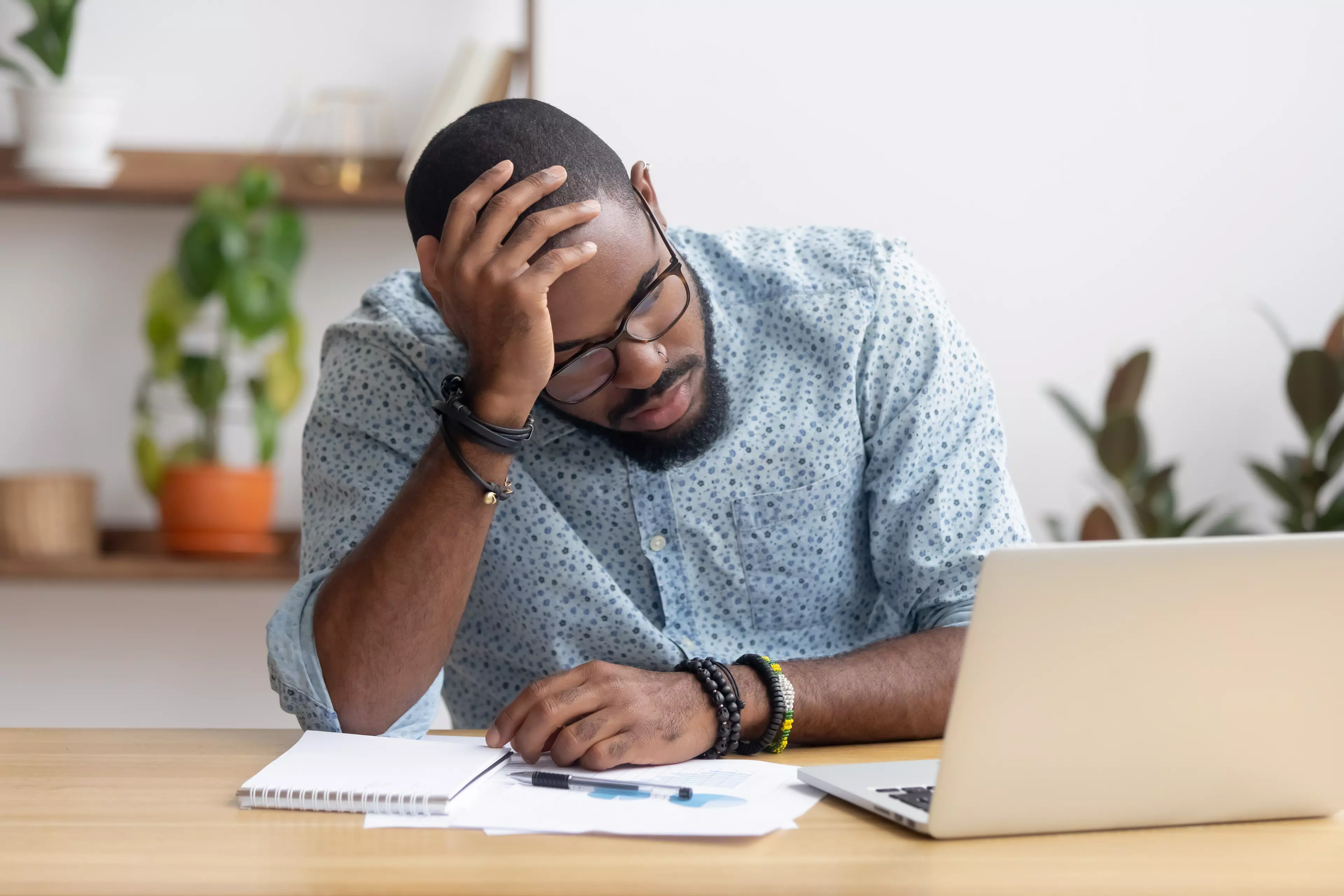 Sad man resting his head on hand in front of a laptop