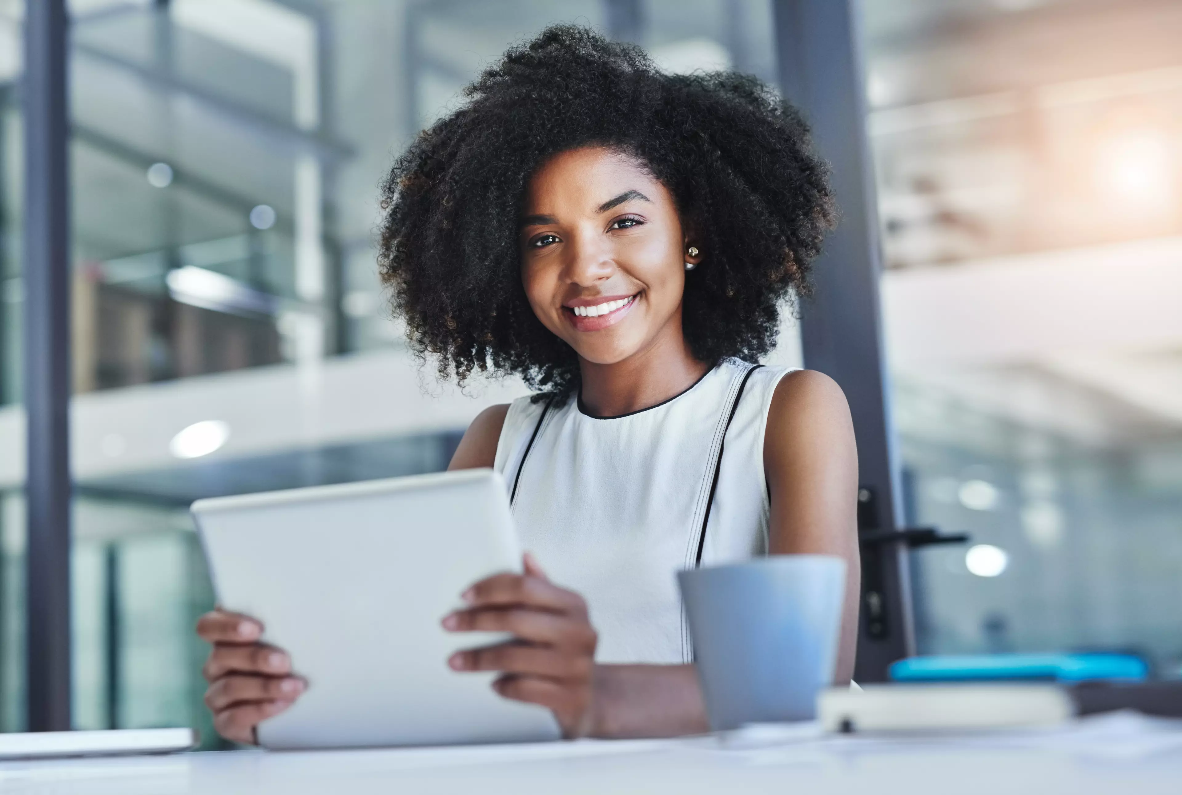 Young, smmiling woman sitting behind a desk with a tablet in her hands.