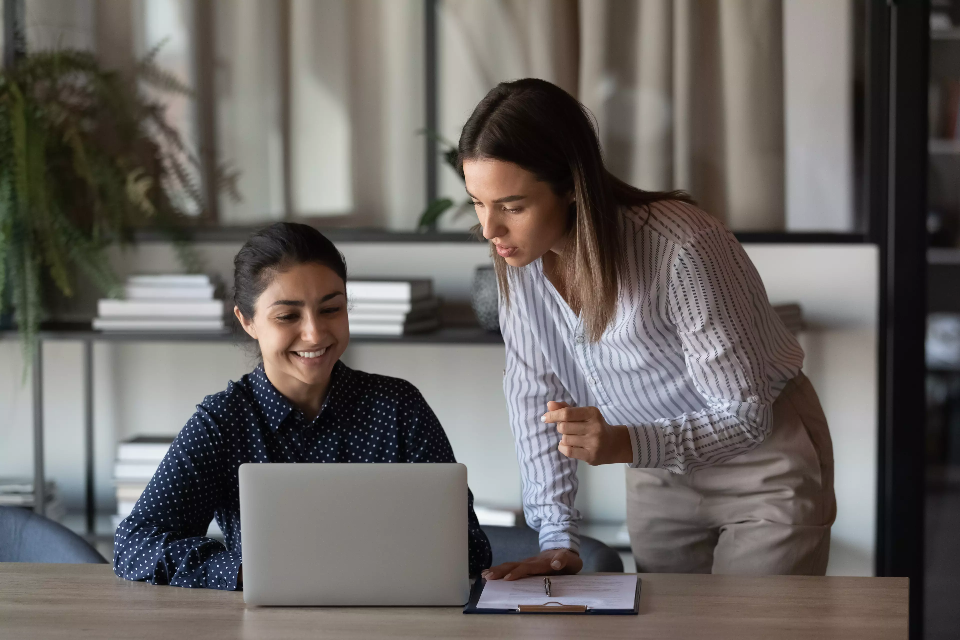 Two young women in the office environment, looking at the laptop screen.