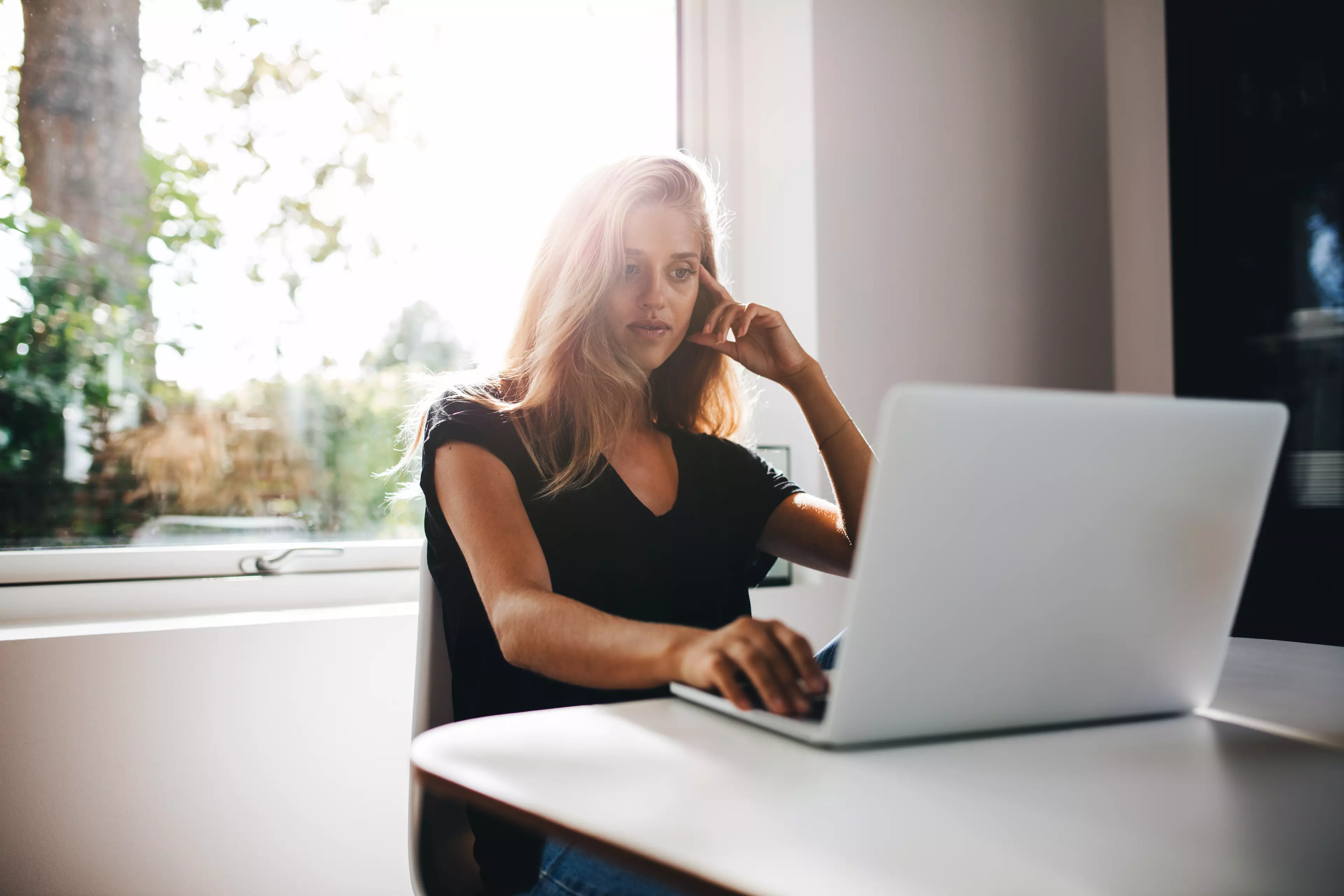  Blonde woman talking on a mobile while sitting in front of a laptop.