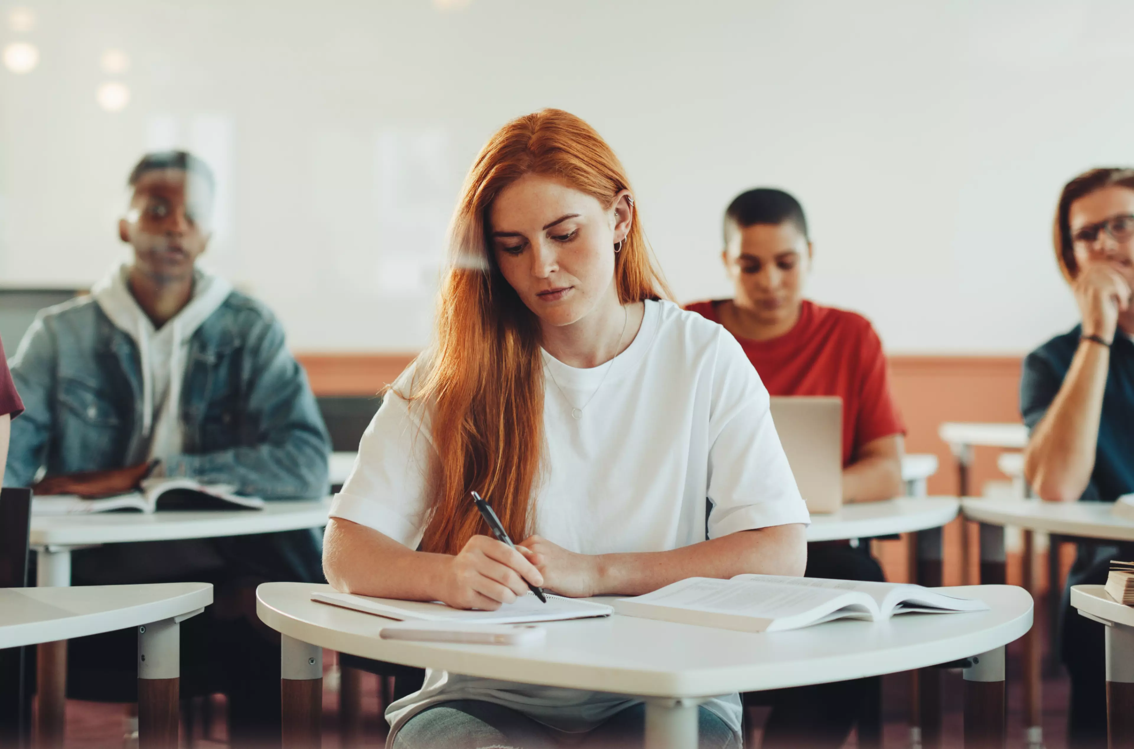 Young read hair woman student sitting behind a desk, taking notes.