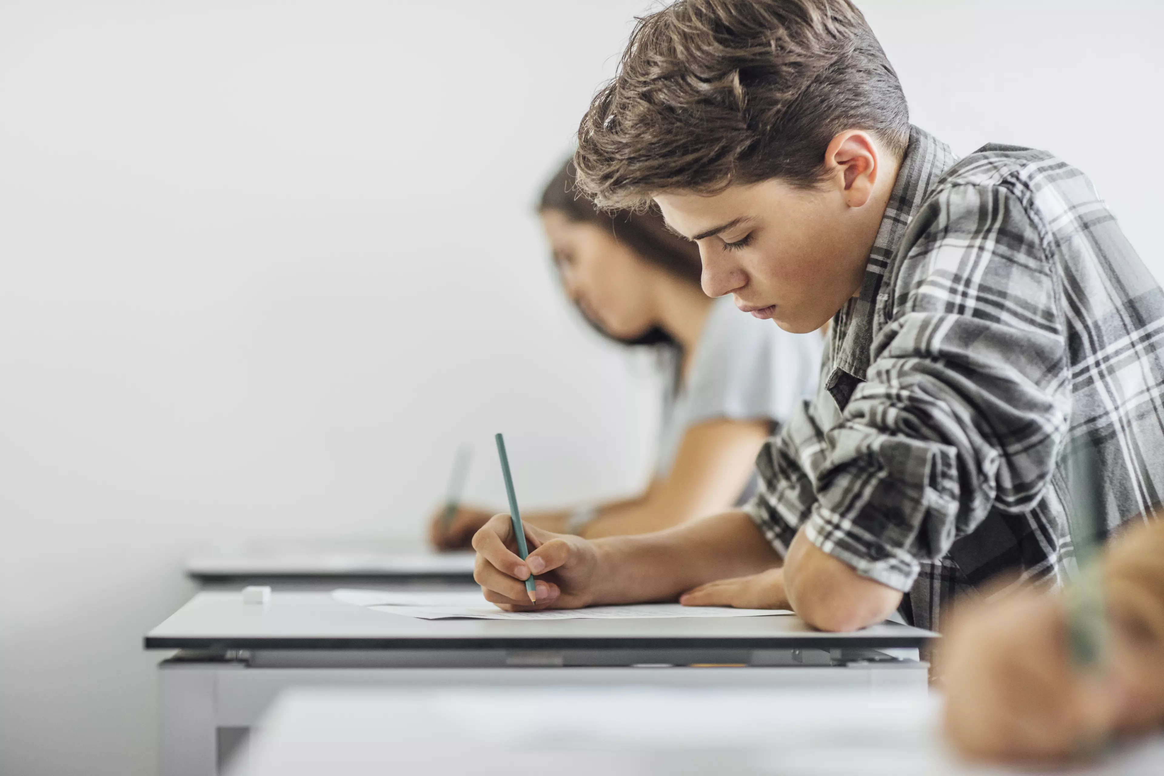 Teenager in the classroom, sitting behind a desk and writing a test