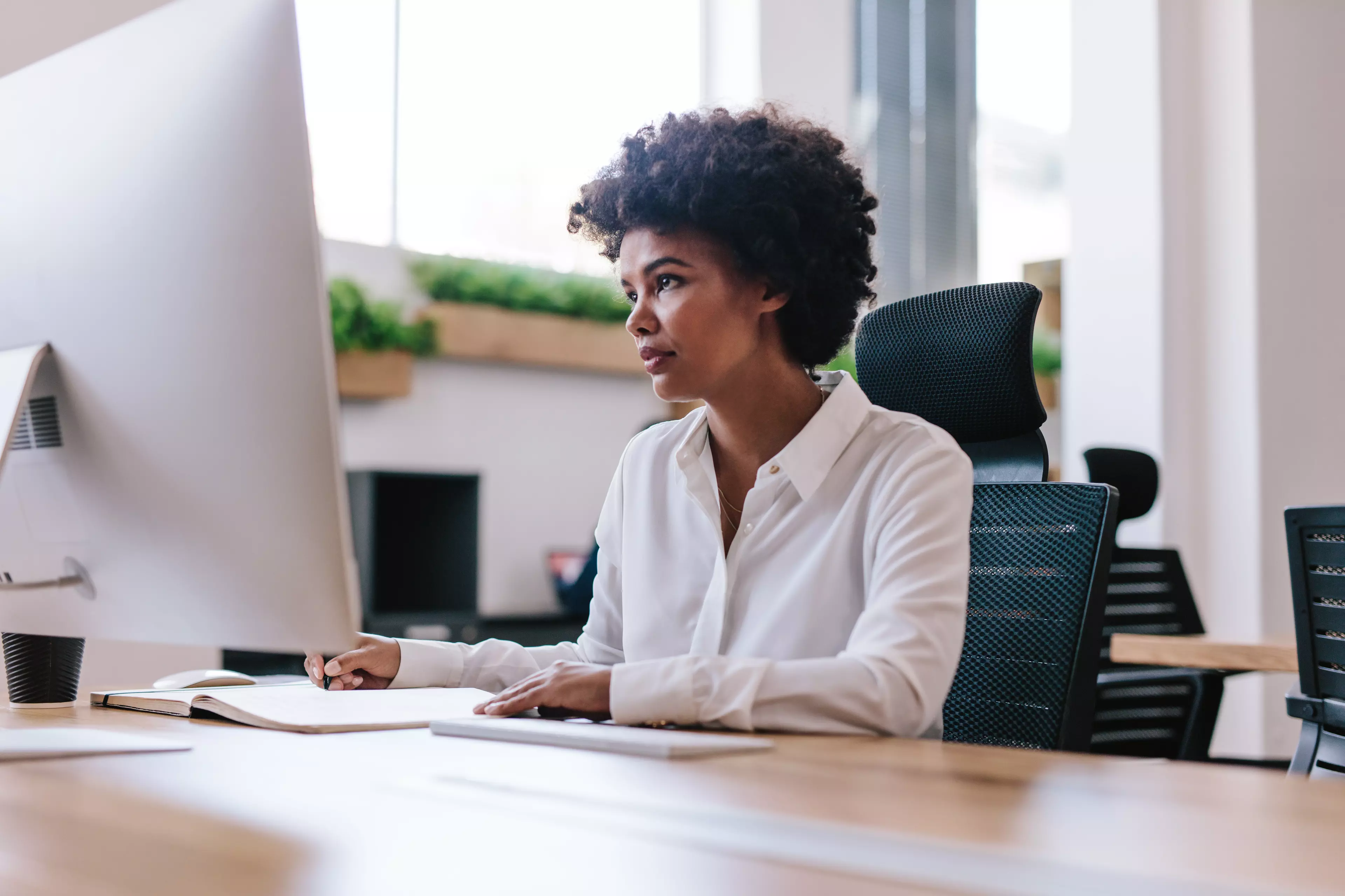 Woman sitting in front of a computer in the office, taking notes.