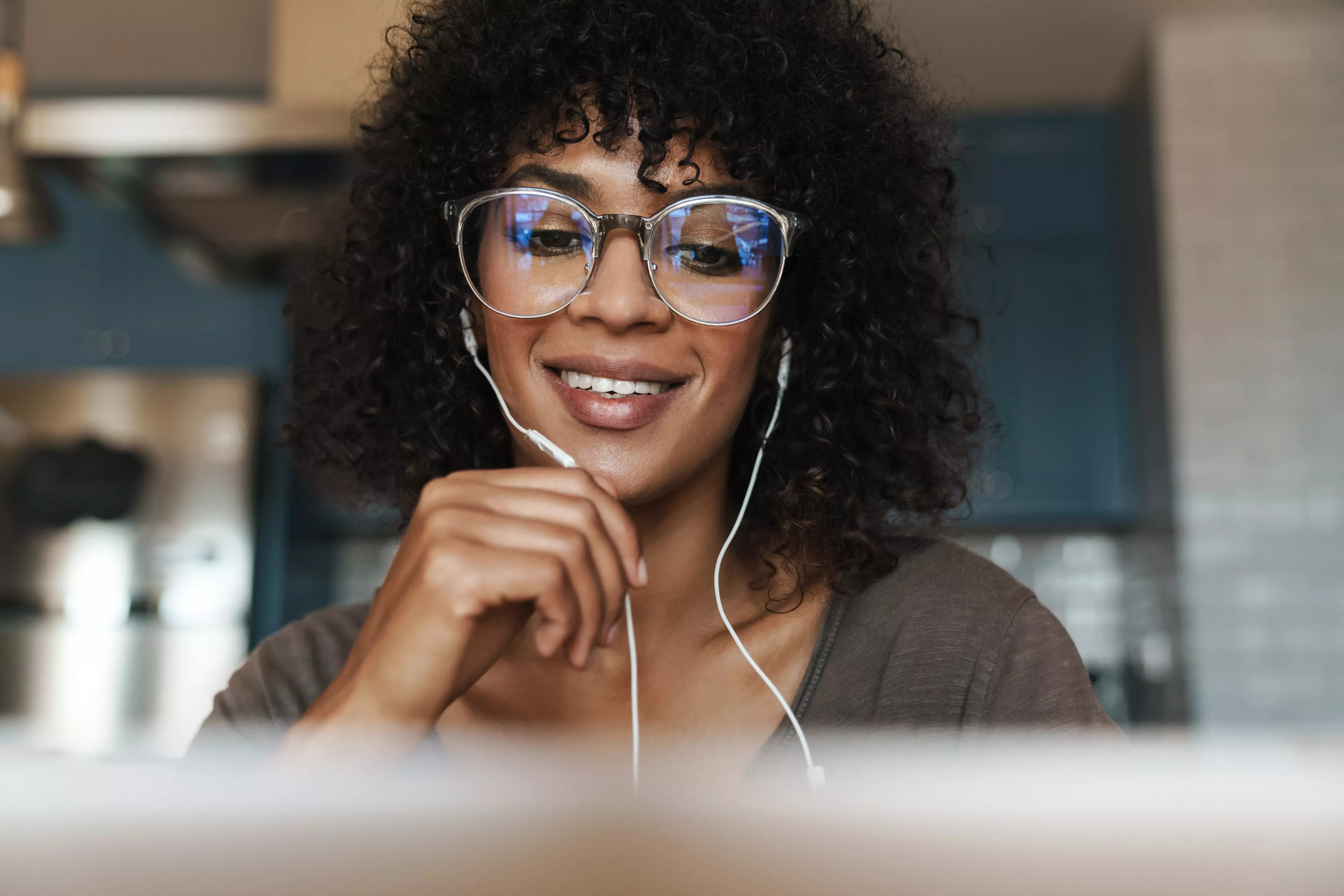 Woman in glasses with long, dark hair, wearing headphones, looking at a computer screen.