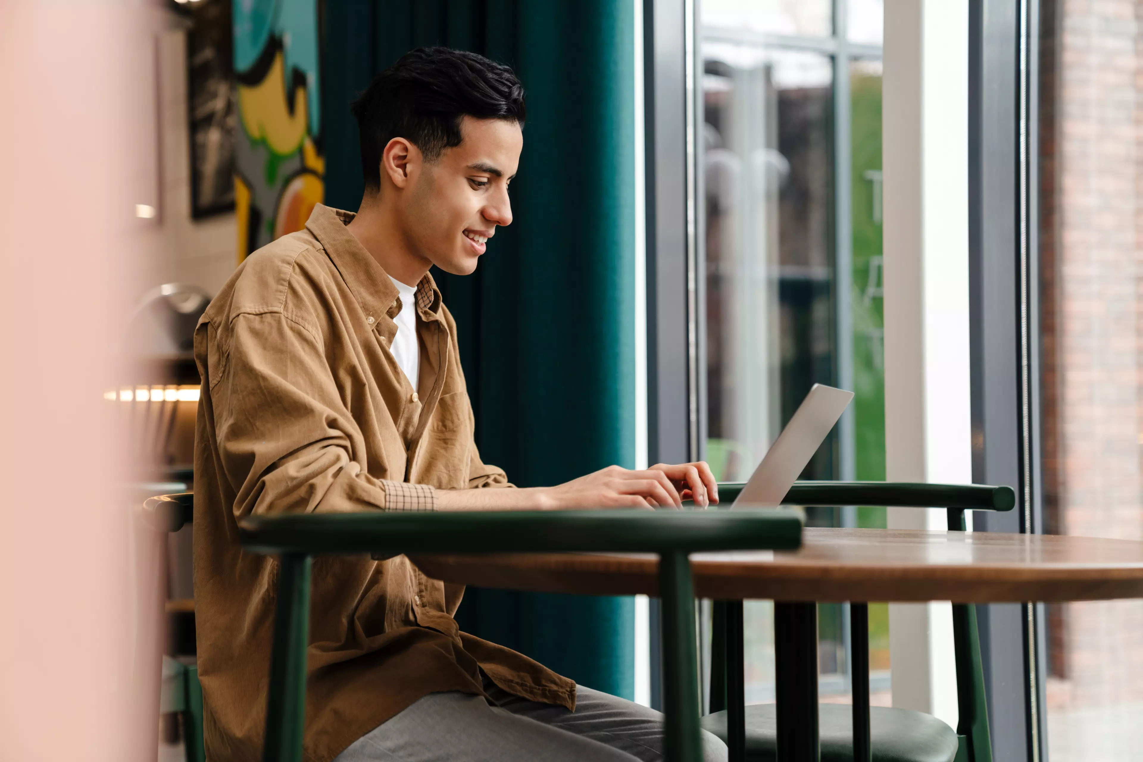  Young man sitting at a table outside, typing on his laptop.