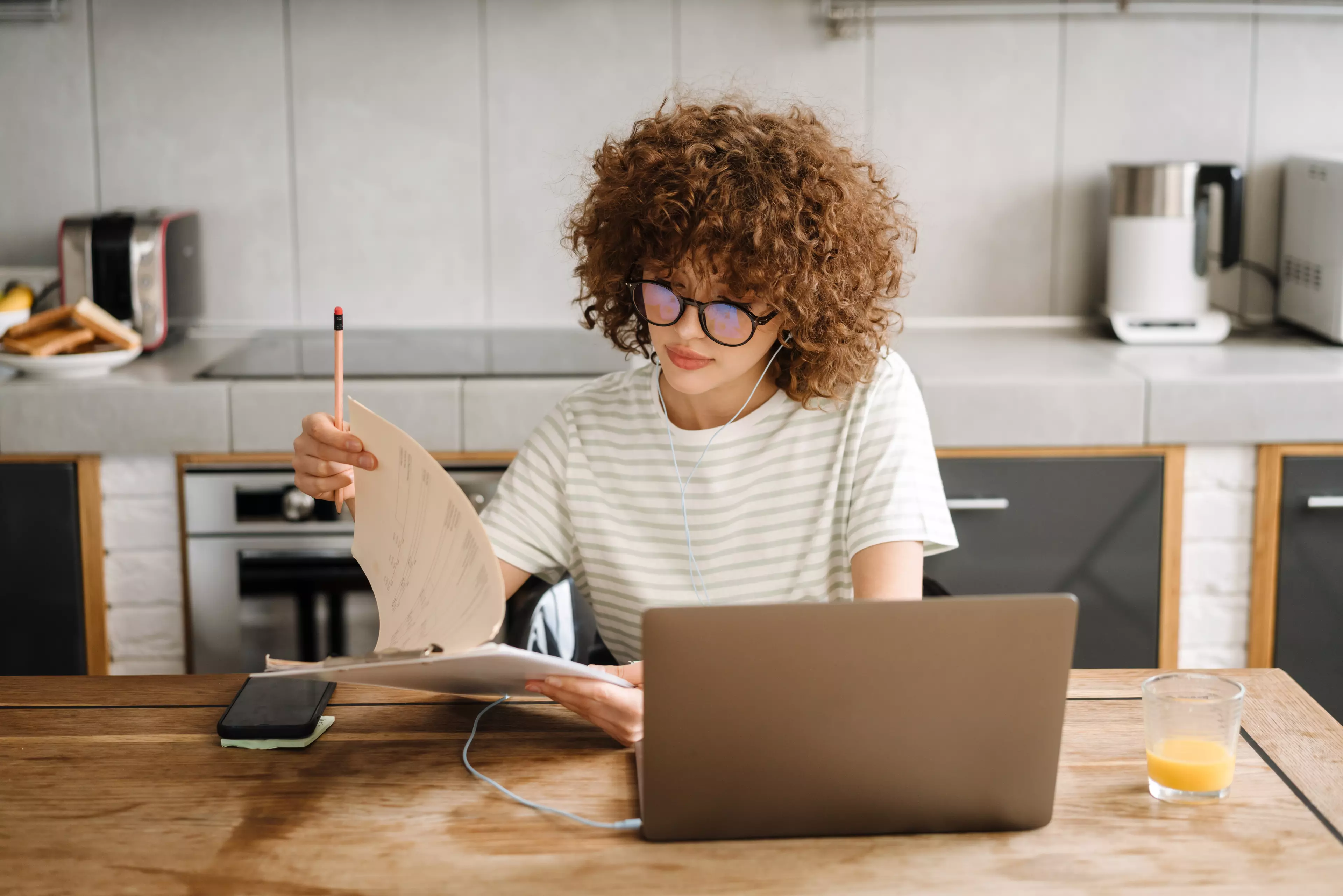  Young girl with curly hair and glasses sitting at a desk, looking at her notebook.