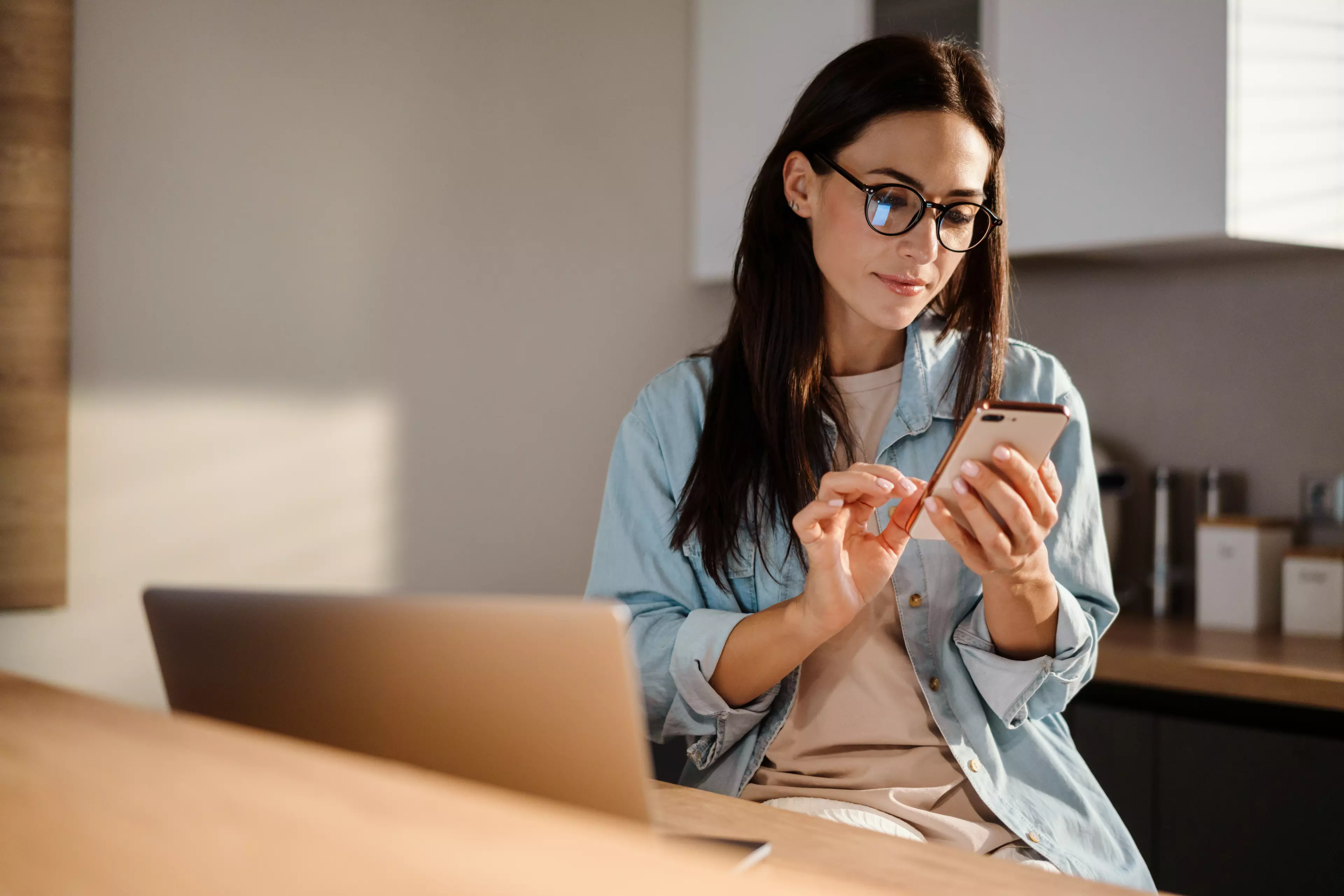  Young, dark-haired woman sitting at a desk, looking at her mobile.