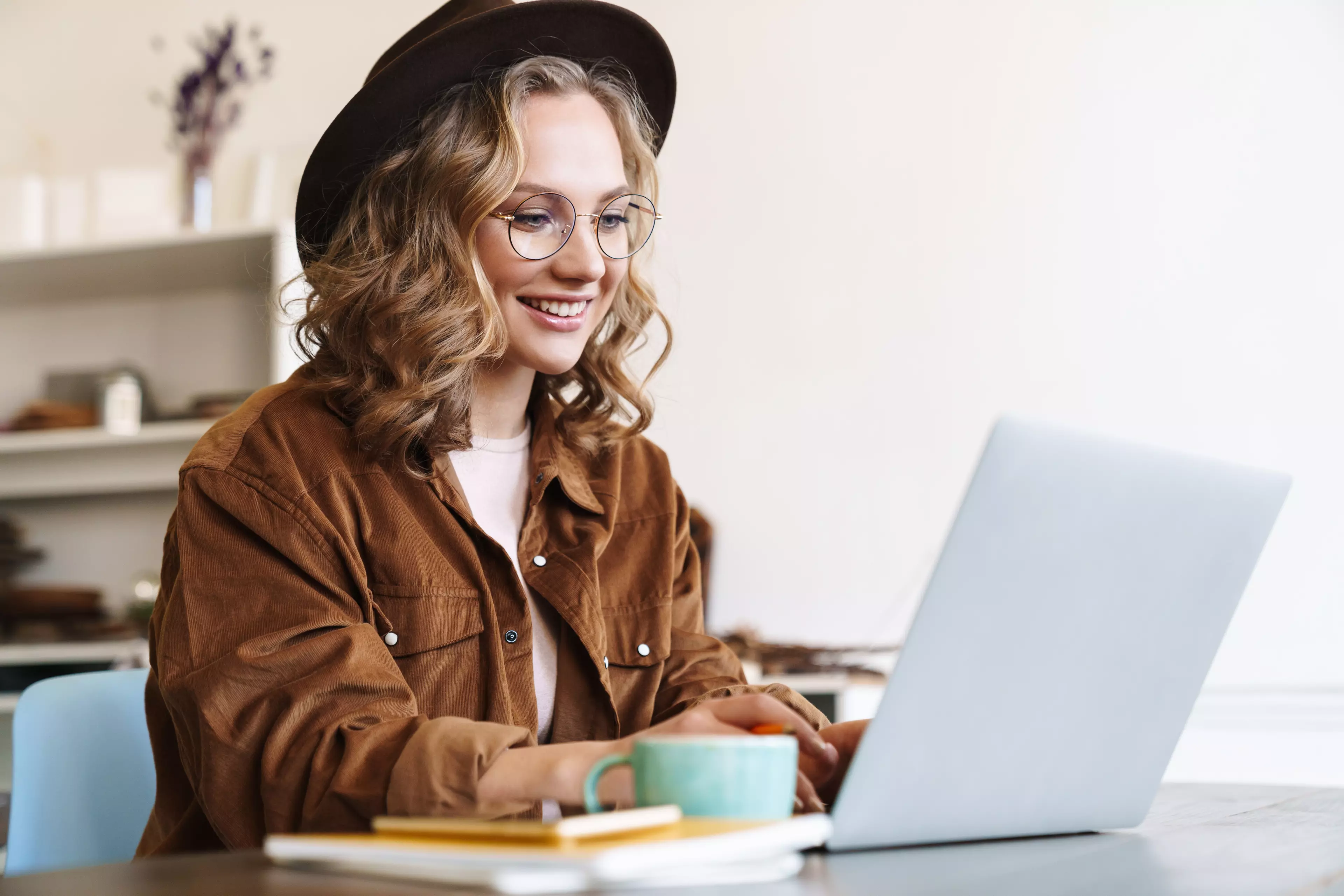  Young woman in a black hat sitting at a desk, typing on a laptop.