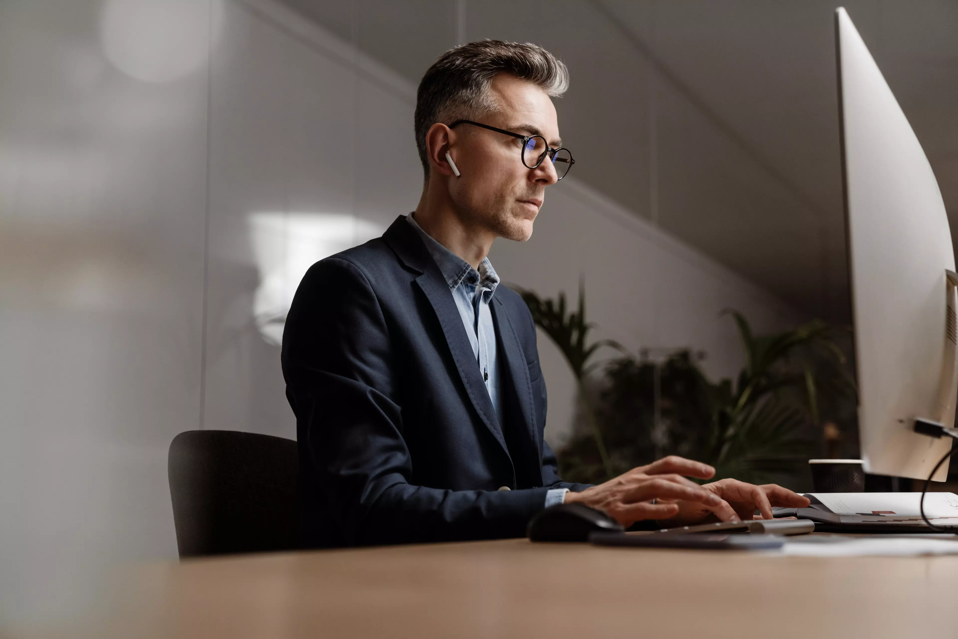  Man in a casual jacket, sitting behind a desk, working on his desktop computer.