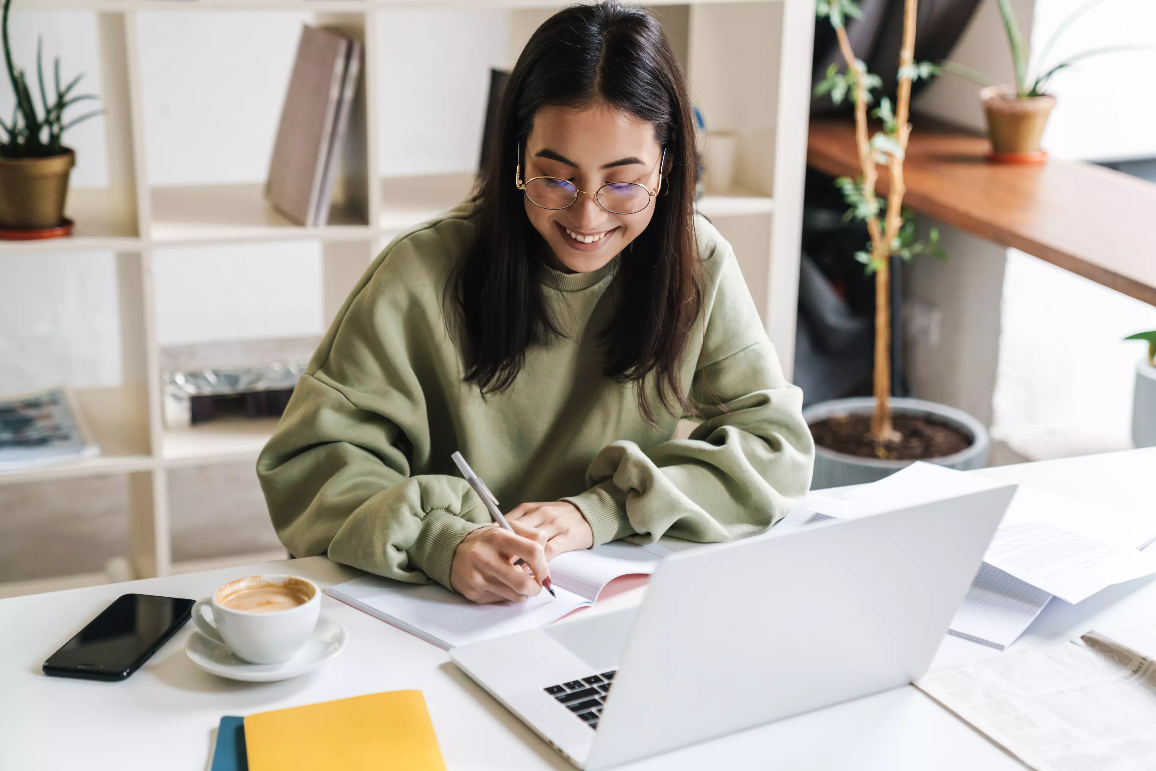  Young dark-haired woman taking notes in front of her laptop.