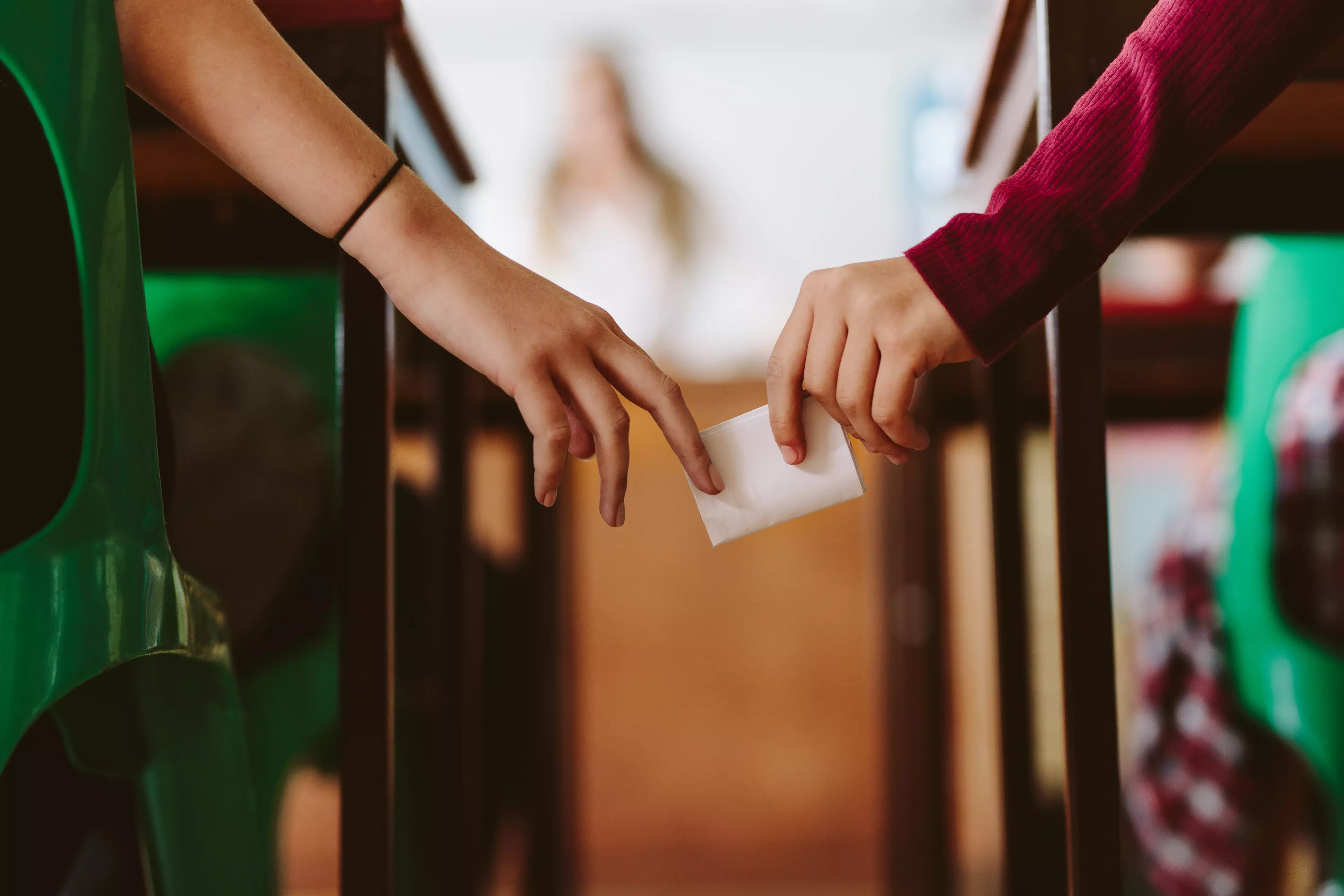 Hands of two young students passing a cheat sheet in the classroom.