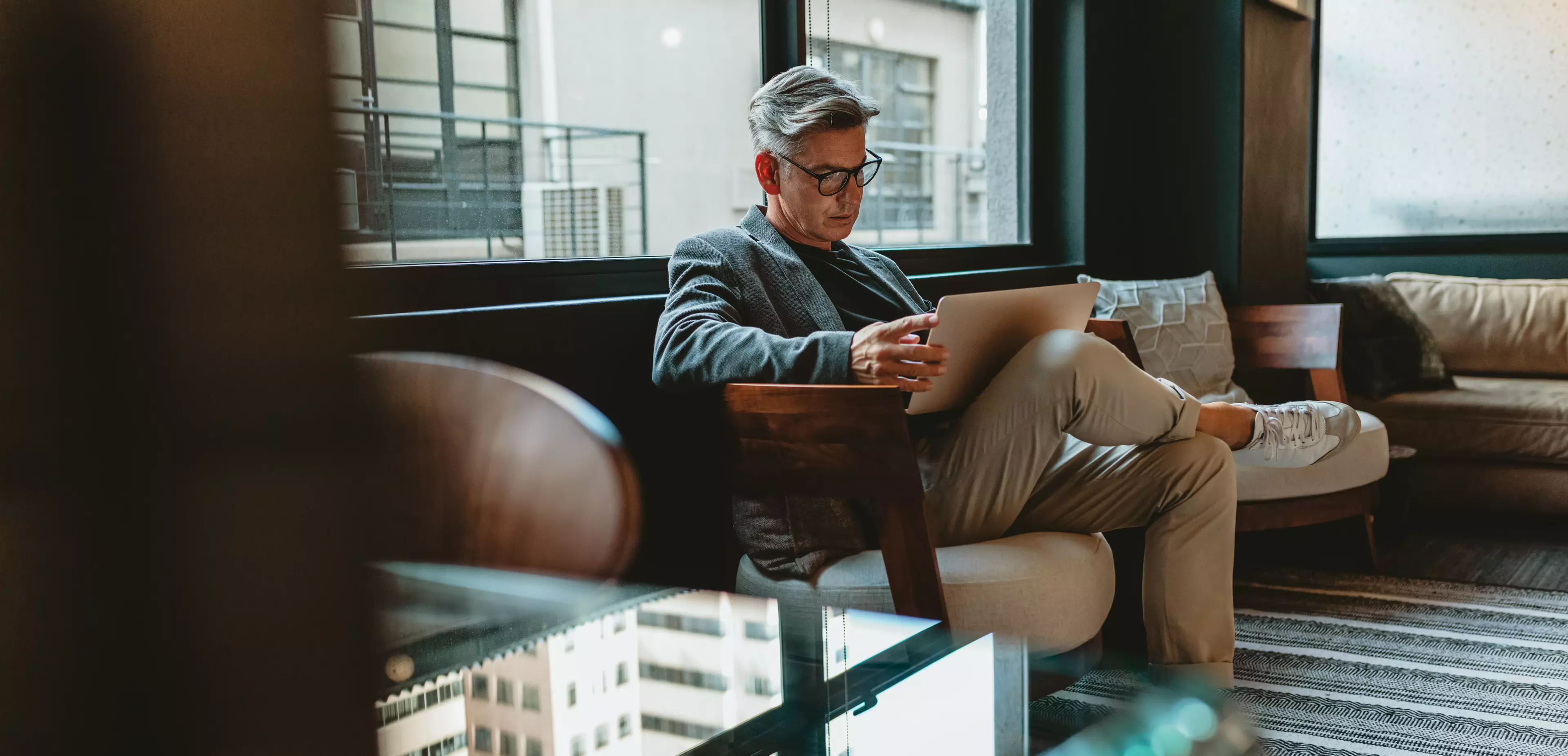 Middle-aged, smart-looking man sitting on a couch with a laptop on his lap.