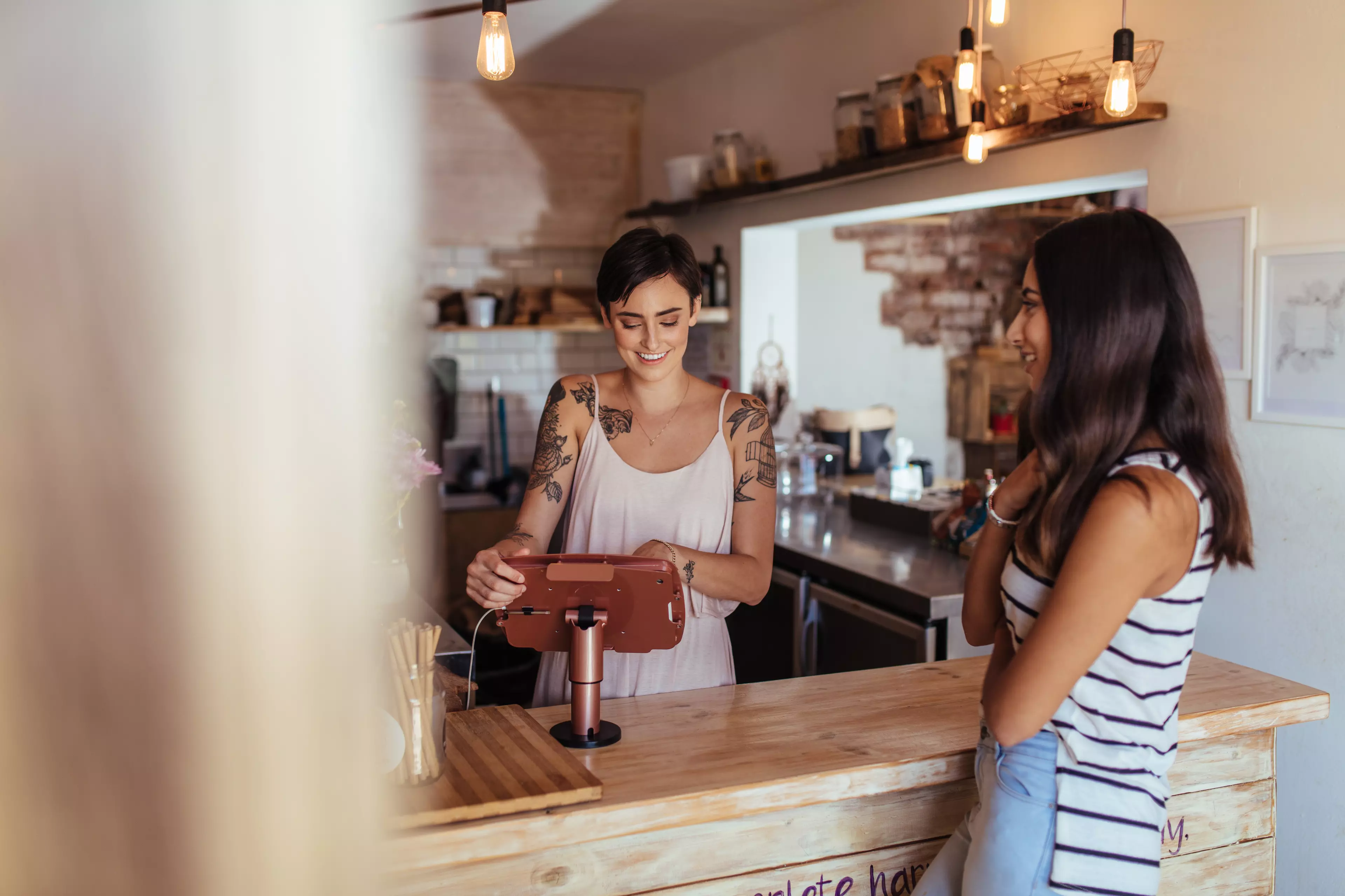  A smiling young woman behind a bar counter serving a client.