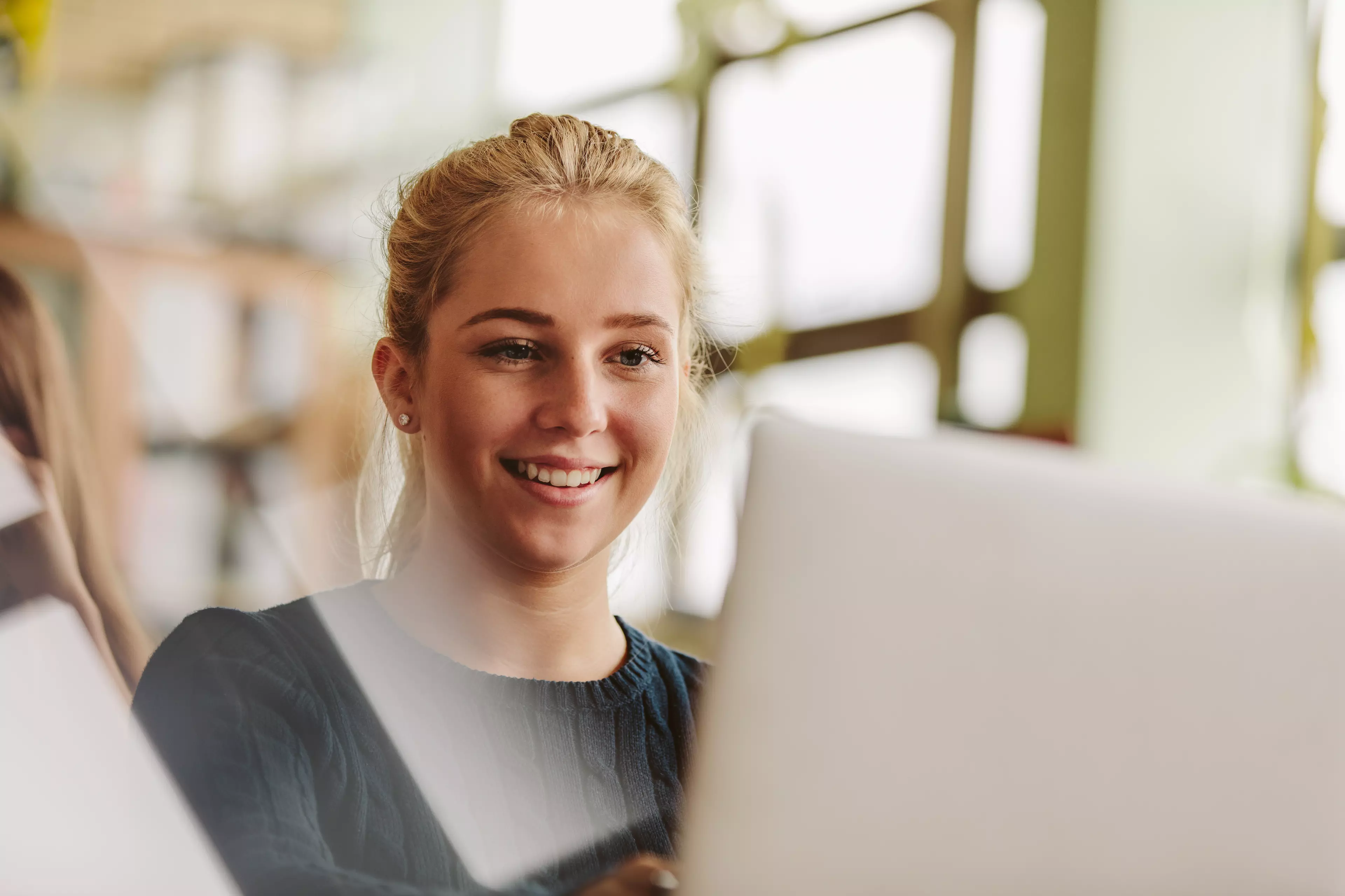 Young, blonde woman smiling looking at a computer screen.