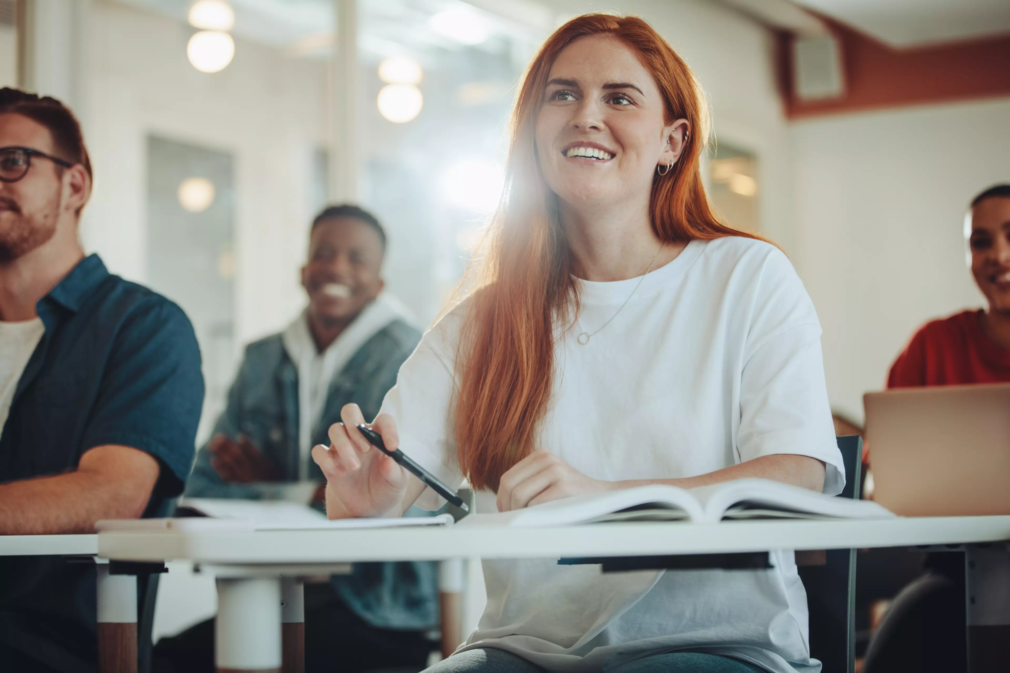  Young, smiling, red-haired woman sitting in a classroom with her peers.